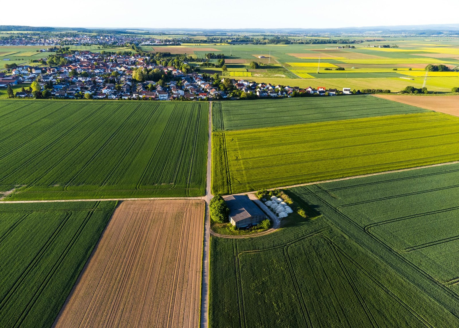 A scenic aerial view showcasing lush green fields and a distant village under a clear sky, ideal for agriculture topics.