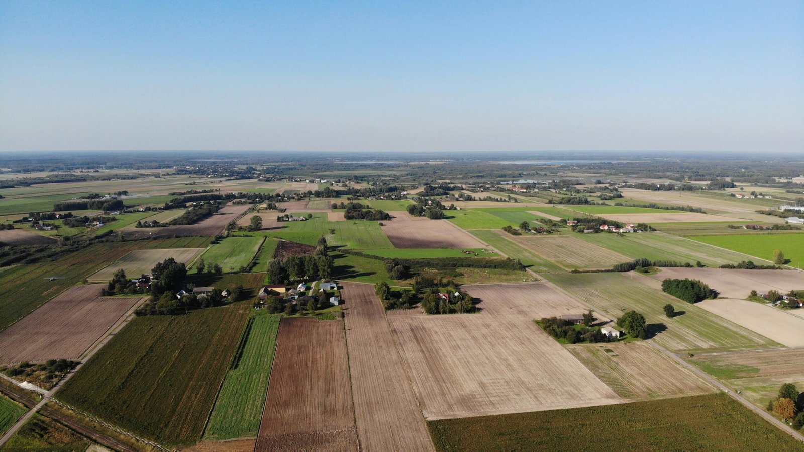Expansive aerial view of farmland in Nadrybie Ukazowe, showcasing lush fields and rural landscape under a clear sky.