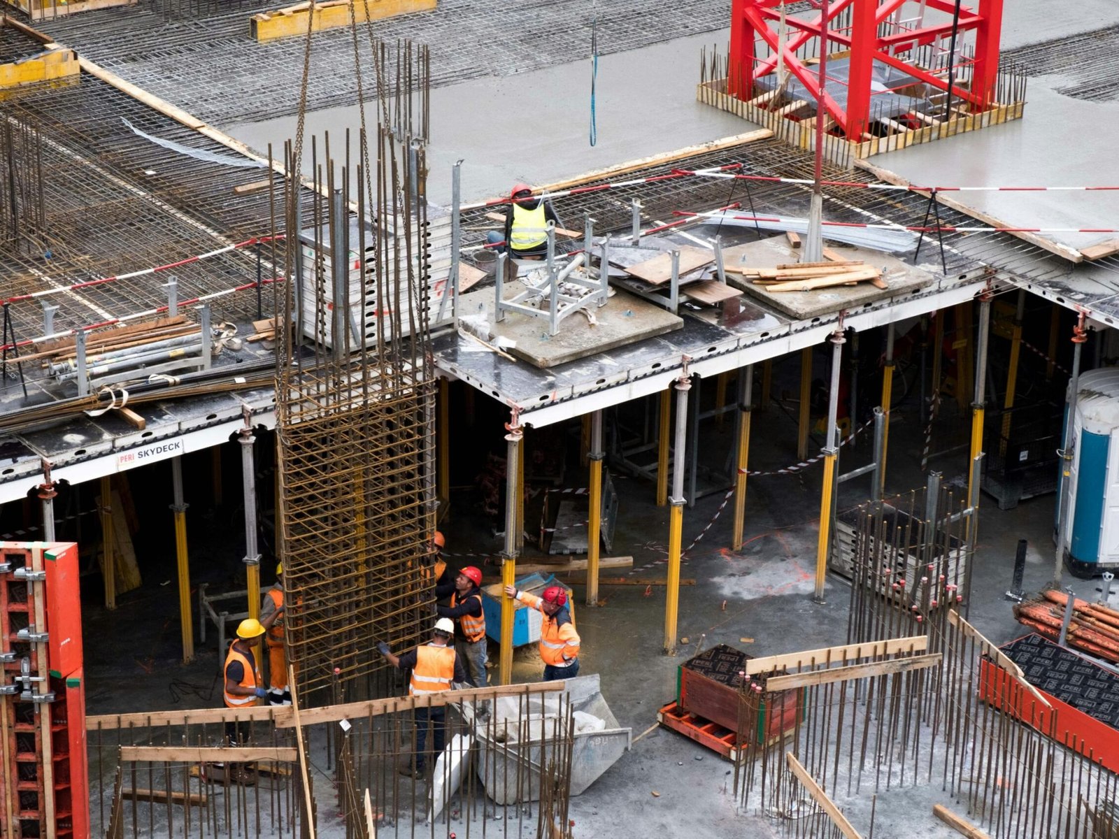 Workers in high visibility gear at a busy construction site with scaffolding and steel frames.