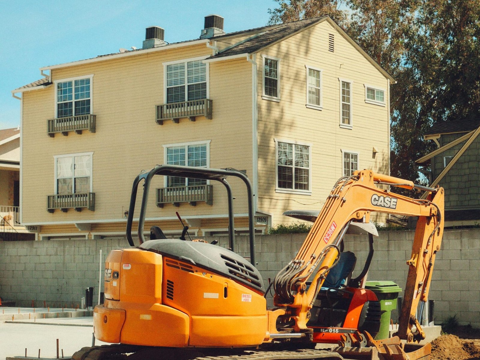 Yellow excavator at residential construction site in Los Angeles with homes in background.