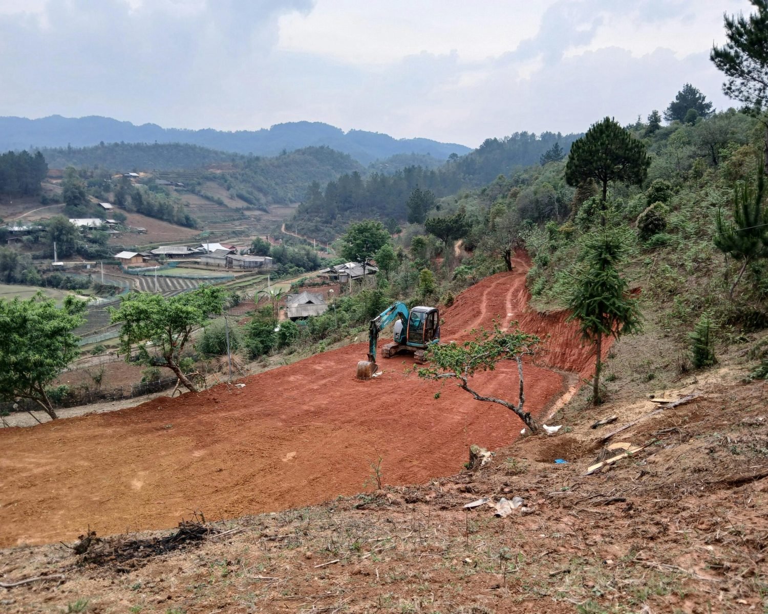 Excavator operating on a terraced hillside with scenic mountain views in the background.