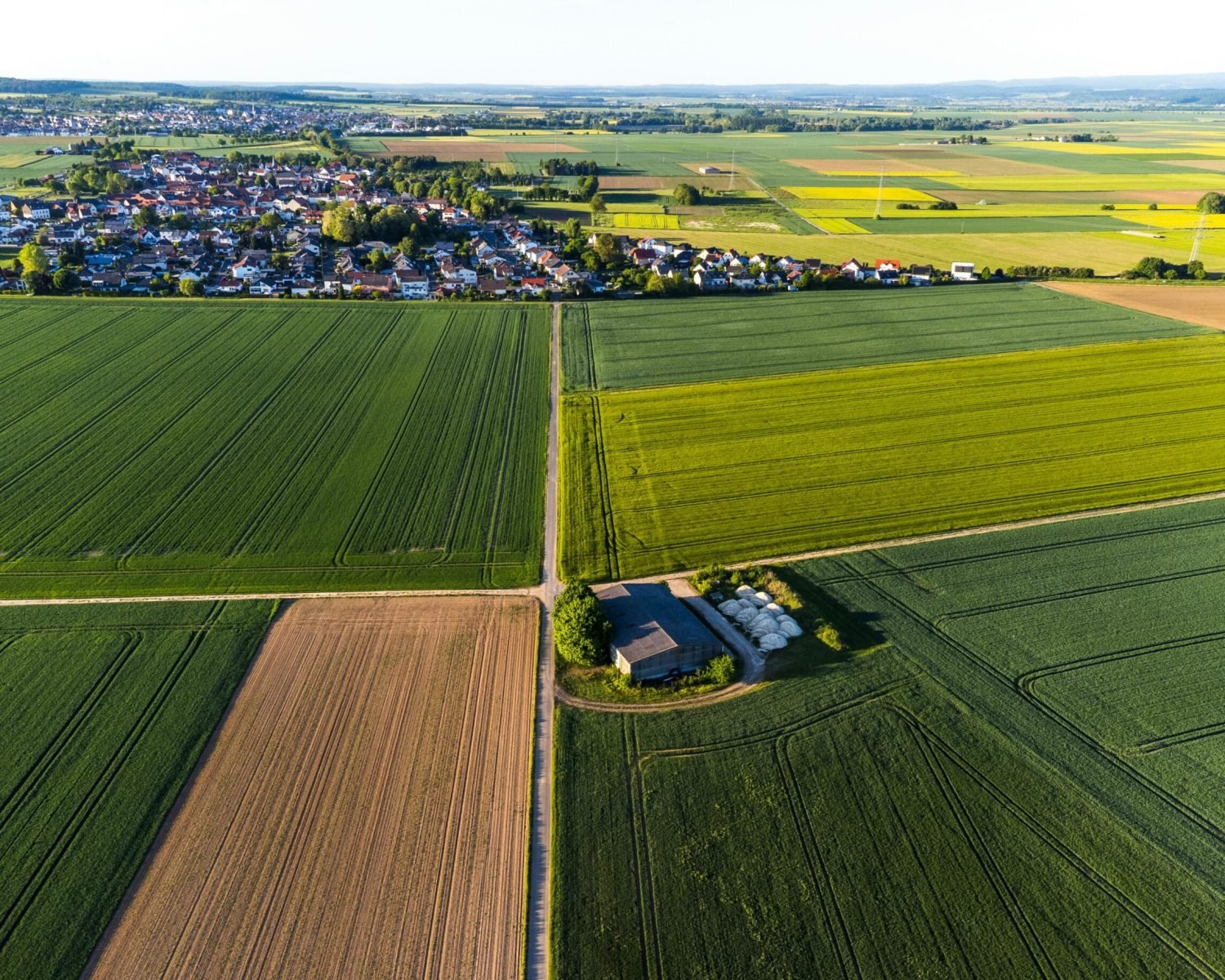 A scenic aerial view showcasing lush green fields and a distant village under a clear sky, ideal for agriculture topics.