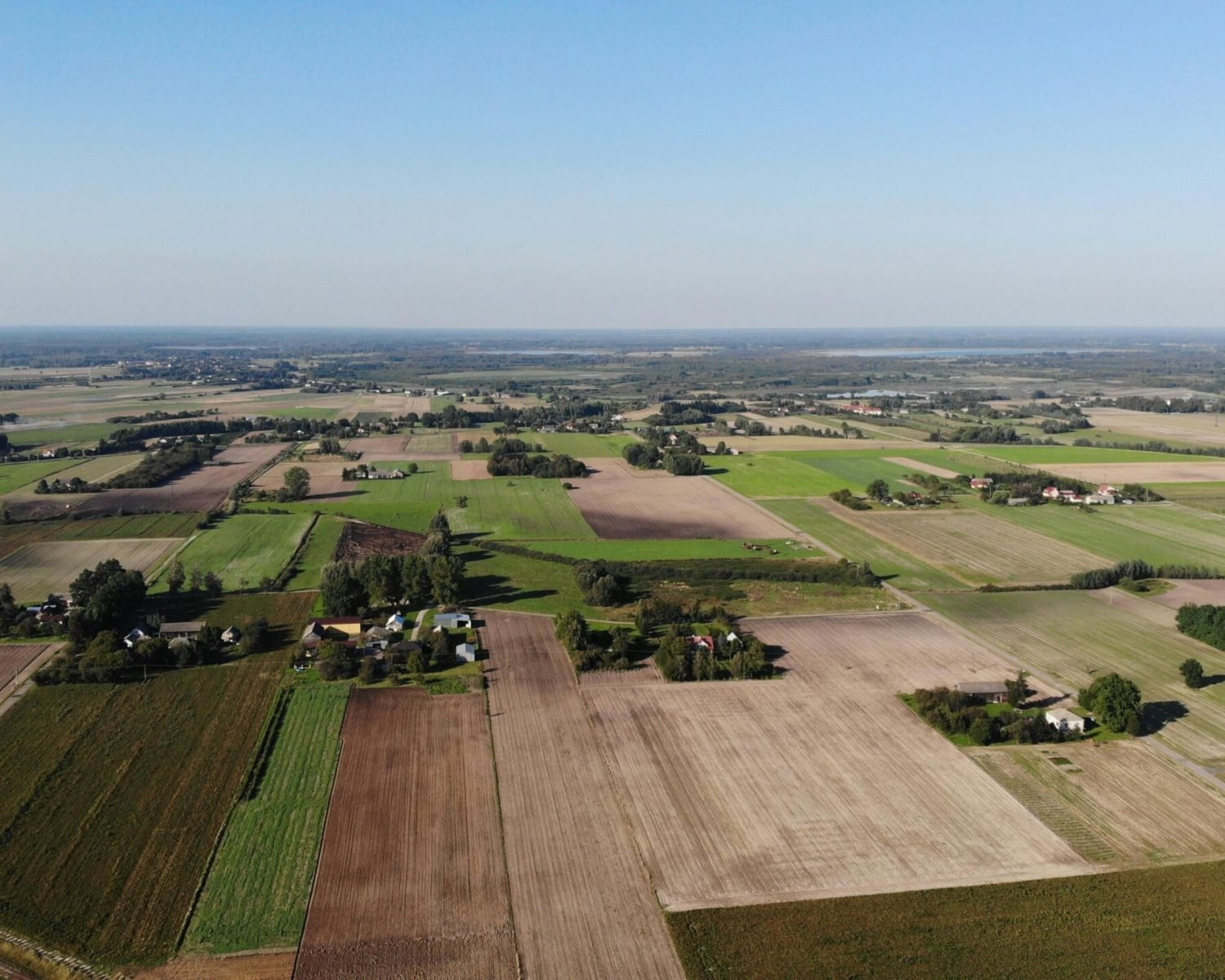 Expansive aerial view of farmland in Nadrybie Ukazowe, showcasing lush fields and rural landscape under a clear sky.