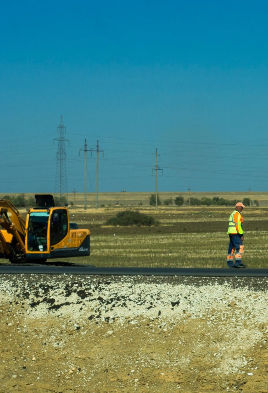 Man working on a road construction site with an excavator outdoors.