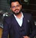 Stylish man in a dark suit smiling confidently indoors.